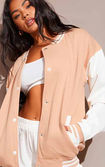 Woman wearing a beige and white varsity jacket over a white top and pants.