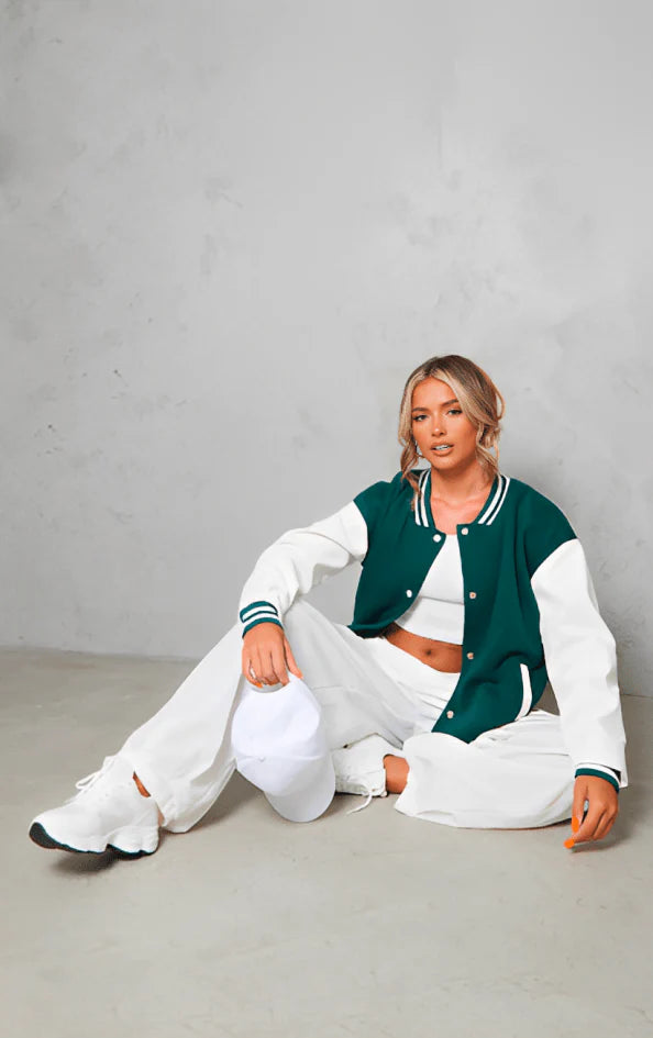 Woman wearing a green and white varsity jacket with a plain background