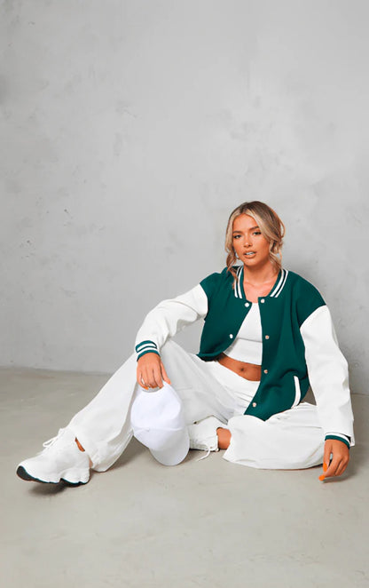 Woman wearing a green and white varsity jacket with a plain background