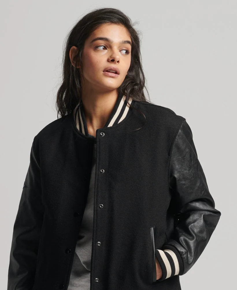 Person wearing a black varsity jacket with leather sleeves on a plain background