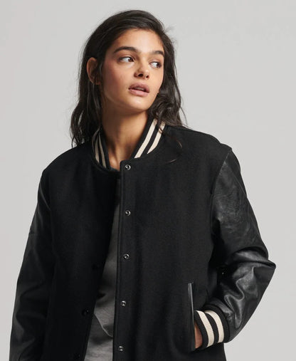 Person wearing a black varsity jacket with leather sleeves on a plain background