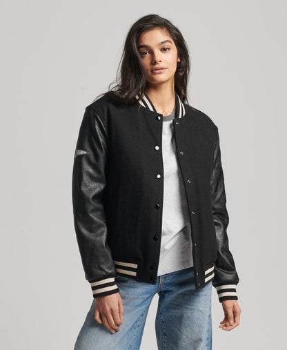 Person wearing a black varsity jacket with leather sleeves on a gray background