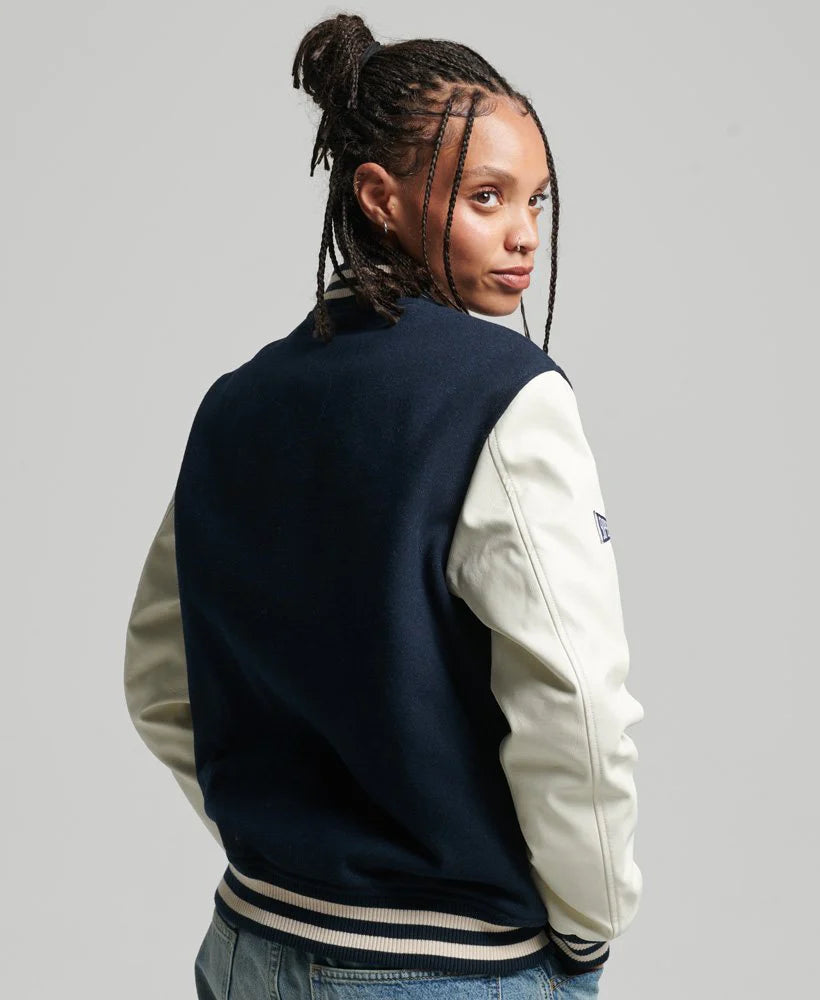 Person wearing a navy and beige varsity jacket on a gray background