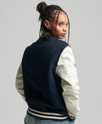 Person wearing a navy and beige varsity jacket on a gray background